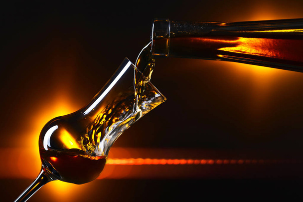 Alkoholtartalmú ital öntése egy pohárba sötét alapon - Fotó, kép