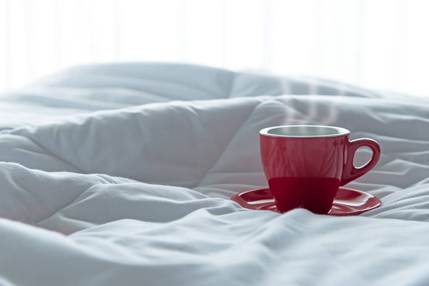 Fresh morning coffee in red cup on the bed. - Φωτογραφία, εικόνα