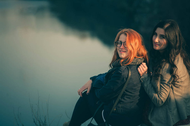 Girlfriends on the shore of the lake at sunset. Happy girl friends hugging in a forest at sunset. - Photo, image