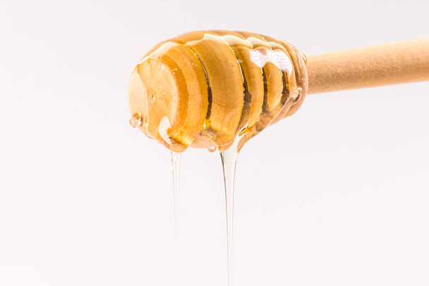 Honey dripping from a wooden honey dipper isolated on white - Photo, Image