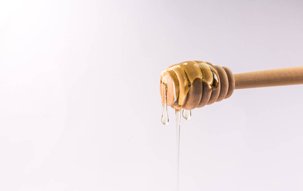 Honey dripping from a wooden honey dipper isolated on white - Photo, image