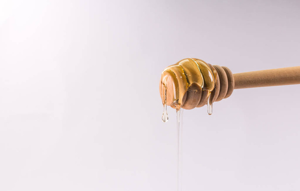 Honey dripping from a wooden honey dipper isolated on white - Foto, Imagem