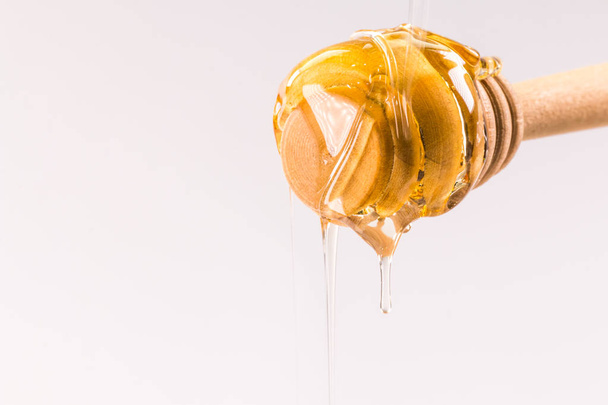 Honey dripping from a wooden honey dipper isolated on white - Foto, immagini