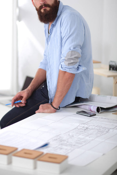 Portrait of male designer in hat with blueprints at desk - Фото, изображение