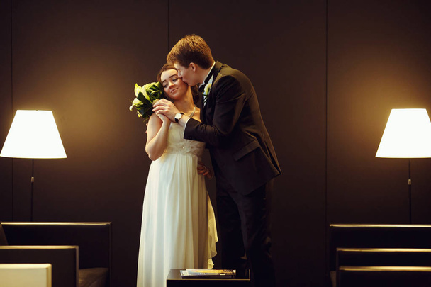 Groom kisses bride's cheek holding her hand with a wedding bouqu - Фото, зображення