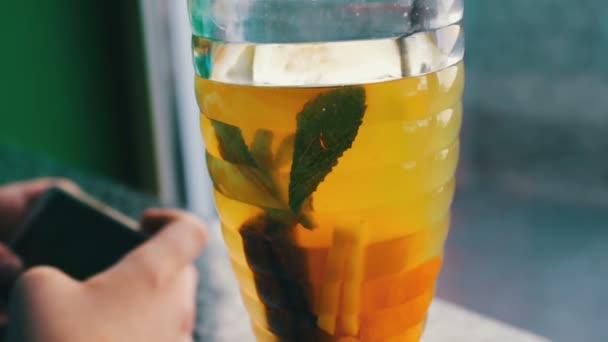 A boy playing on a smartphone in a cafe next to lemon tea with cinnamon - Footage, Video