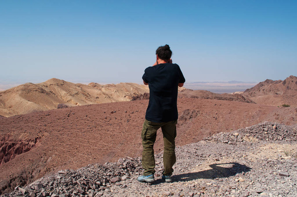 Middle East: a man taking pictures of desertic landscape on the road that links the Dana Biosphere Reserve, Jordan's largest nature reserve, to the archaeological Nabataean city of Petra - Foto, afbeelding