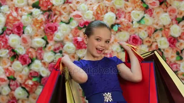 Childrens shopping. Portrait of blonde little girl in blue dress, background of bright floral wall - Imágenes, Vídeo
