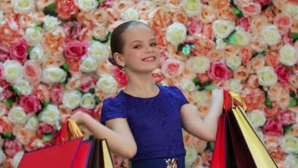 Childrens shopping. Portrait of beauty little girl in blue dress, background of bright floral wall - Imágenes, Vídeo