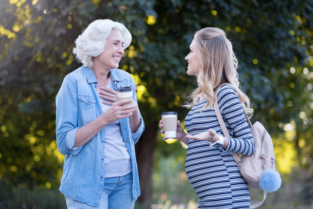 Joyful pregnant woman enjoying conversation with aged mother outdoors - Zdjęcie, obraz
