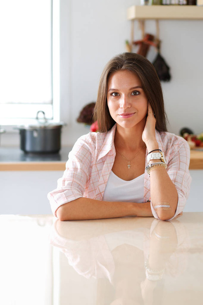 Mujer joven sentada cerca de escritorio en la cocina - Foto, imagen