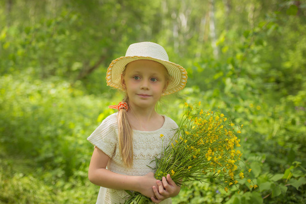 Portrait cute little girl in hat with bouquet of wildflowers on summer day - 写真・画像