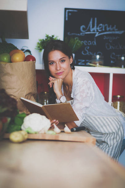 Young woman reading cookbook in the kitchen, looking for recipe - Foto, immagini