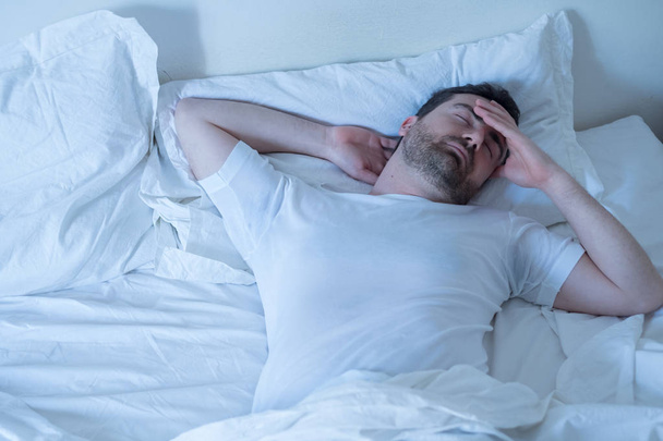 Расстроенный мужчина пытается спать в своей постели ночью
 - Фото, изображение