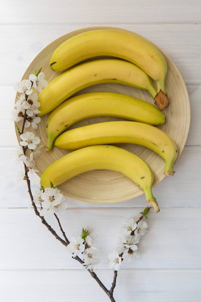 бананы и цветение абрикоса в деревянной пластине на фоне белого дерева
 - Фото, изображение