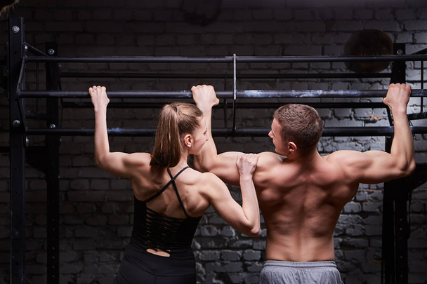 Rear photo of young attractive caucasian crossfit man and woman while working out in gym - Photo, Image
