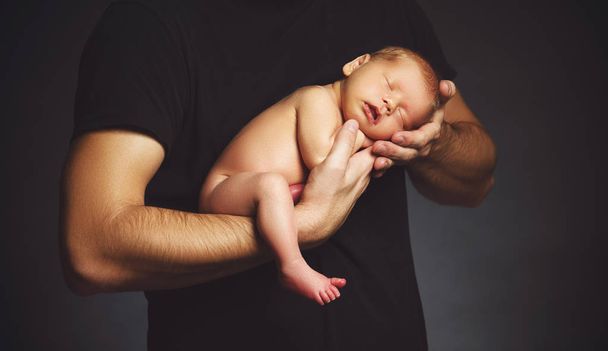 Vastasyntynyt vauva isänsä käsissä pimeässä
 - Valokuva, kuva