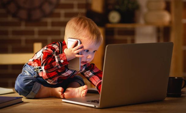 käsite vauva poika työskentelee tietokoneella ja puhuu puhelimessa
 - Valokuva, kuva