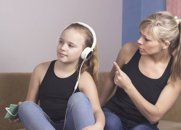 Beautiful woman is scolding her teenage daughter, girl is listening to music in headphones and ignoring her mom - Foto, Bild