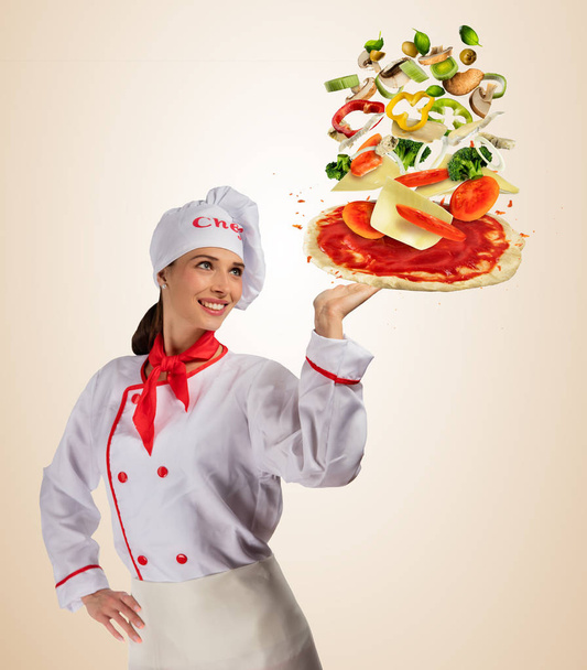 Young woman chef with Flying ingredients on pizza dough - Foto, immagini