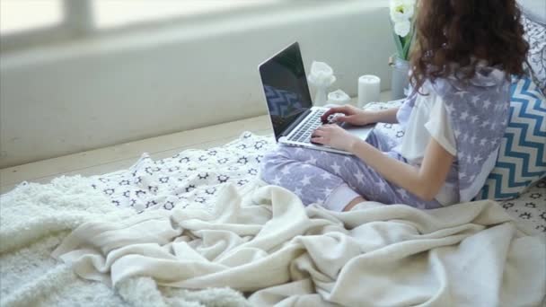 Young woman writes a message on a laptop in the bedroom. - Video