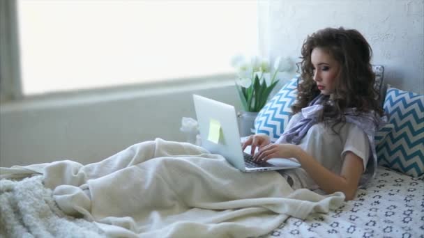 Молода жінка лежить на ліжку в спальні і спілкуватися в чаті з друзями в Інтернеті. - Кадри, відео