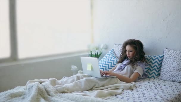 Mooie vrouw ligt op bed in en werkt op laptop in de ochtend. - Video