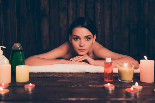 Расслабленная молодая женщина лежит в спа-салоне со свечами и лосьонами
 - Фото, изображение