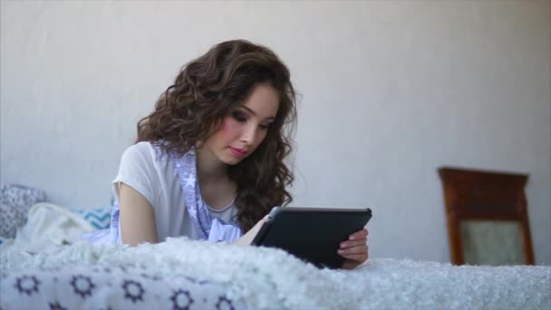 Молодая женщина разговаривает с друзьями с помощью планшета во время лежания в постели в спальне
. - Кадры, видео