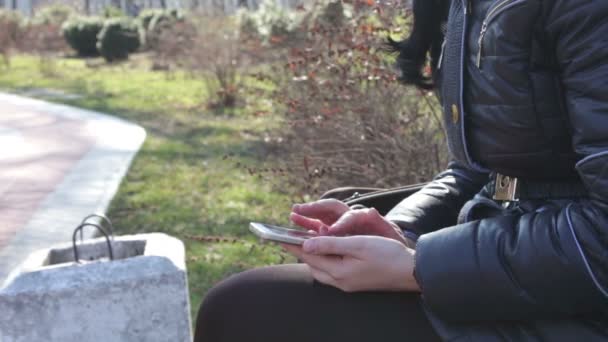Tyttö tulostaa viestin ja selaa sivuja älypuhelimella kevätpuistossa
 - Materiaali, video