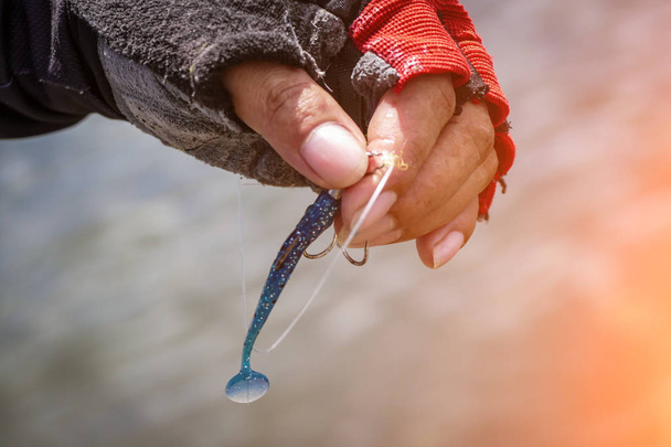 Рыбак привязывает рыболовный крючок к приманке резинового червя
 - Фото, изображение