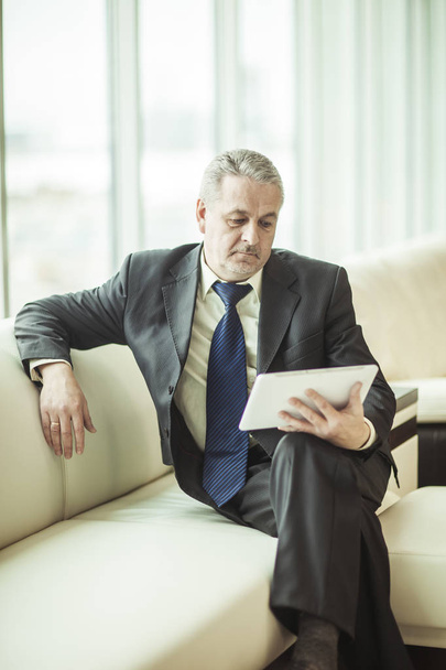 experienced businessman looking at the screen of a digital tablet sitting on sofa in the office - Foto, afbeelding