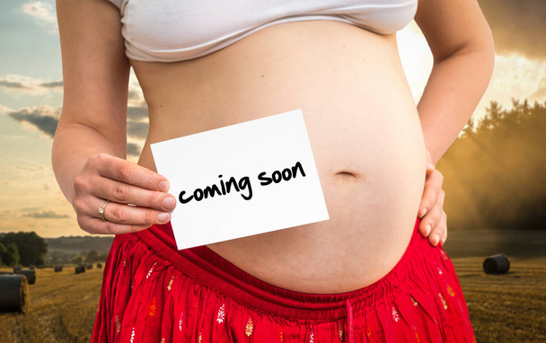 Kobieta w ciąży, trzymając papier z napisem: już wkrótce - Zdjęcie, obraz