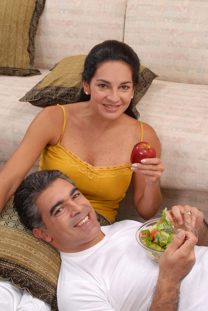 Mid adult couple eating salad and fruit in a living room. - Foto, Bild