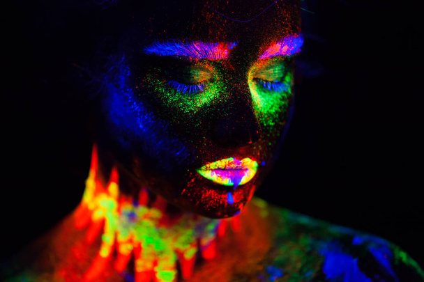 Beautiful extraterrestrial model woman in neon light. It is portrait of beautiful model with fluorescent make-up, Art design of female posing in UV with colorful make up. Isolated on black background - Фото, изображение
