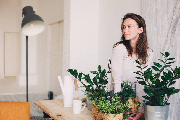 young woman watering flowerpots at home. Casual lifestyle series in modern scandinavian interior - 写真・画像