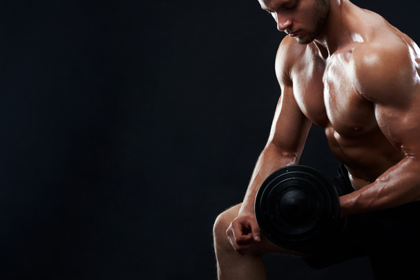 Muscular young man lifting weights on black background - Fotoğraf, Görsel