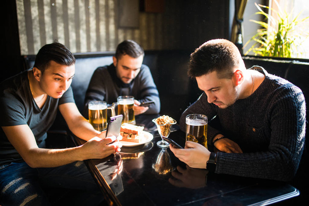 男性の友人がスマート フォンでビールを飲みながら座っているバーやパブ。スマート フォン依存性. - 写真・画像