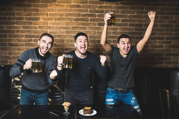 Trois hommes avec le cri de but de bière de leur équipe préférée dans le pub. Pub boire de la bière
. - Photo, image