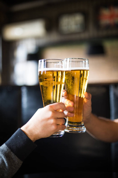 ¡Salud! Primer plano de dos hombres en camisas brindando con cerveza en el mostrador del bar
 - Foto, Imagen