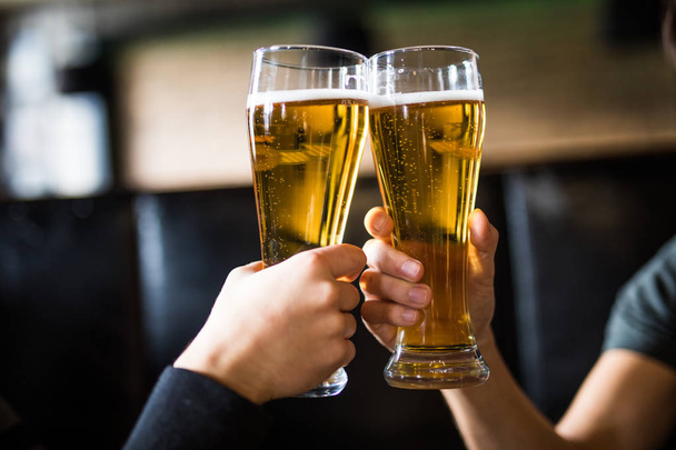Los hombres aplauden con cerveza en vasos en el pub. De cerca.
. - Foto, imagen