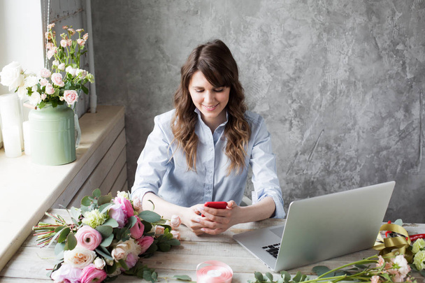 Mosolyogva érett nő virágüzlet Small Business virág üzlet tulajdonosa. Ő használja a telefon és a laptop a megrendeléseket neki áruház. szelektív összpontosít. - Fotó, kép