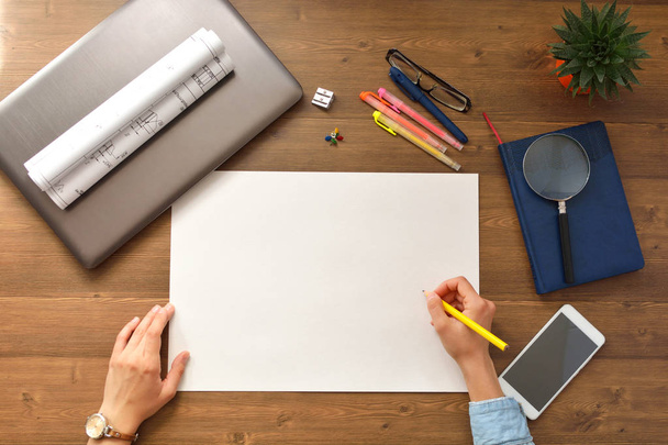 Sheet of clean white paper, designer hands, blueprints, computer, glasses and pot with cactus on a wooden background. - Fotó, kép