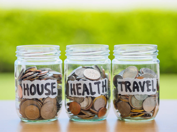 Un sacco di monete in vaso di denaro di vetro sul tavolo di legno. Risparmio per la casa, la salute e il concetto di viaggio
. - Foto, immagini