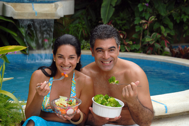 Young couple eating salad behind a swimming pool. - Foto, imagen
