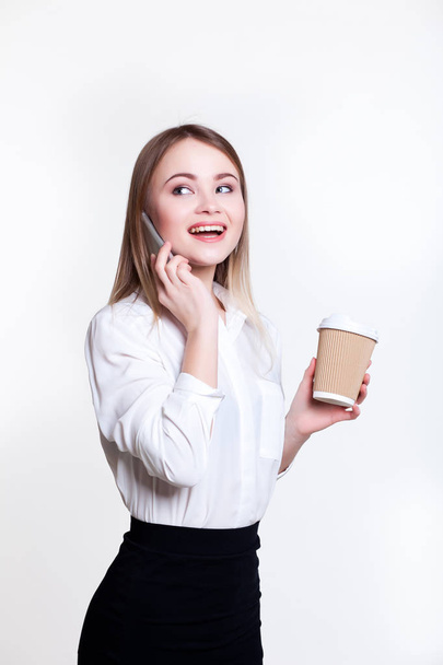 Young attractive business girl on a white background with coffee and phone - Фото, изображение