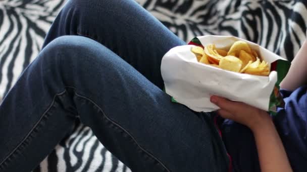 Junge Teenager essen Kartoffelchips mit den Händen auf dem Sofa zu Hause. Fast Food ungesundes Essen - Filmmaterial, Video