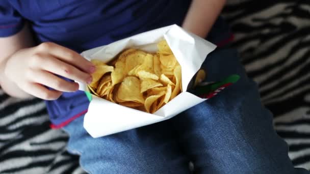 Chlapec dospívající jíst brambůrky s rukama na pohovce v home.fast potraviny nezdravé jídlo - Záběry, video