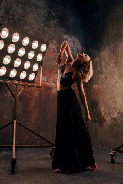 Retrato de una hermosa y atractiva bailarina rubia en el escenario con luces en el fondo del loft bailando danza gratis
 - Foto, imagen