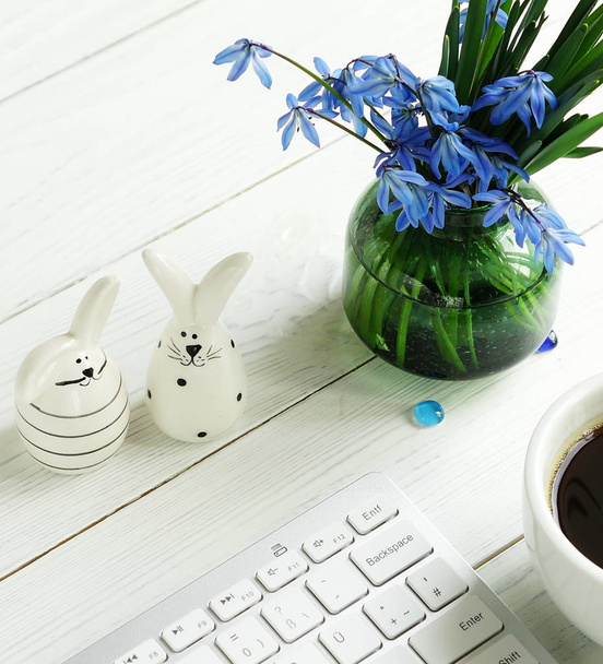 Easter concept. Flat lay office table feminine desk. workspace with laptop, bouquet blue flowers, figures of hares on a white wooden background. - Фото, зображення
